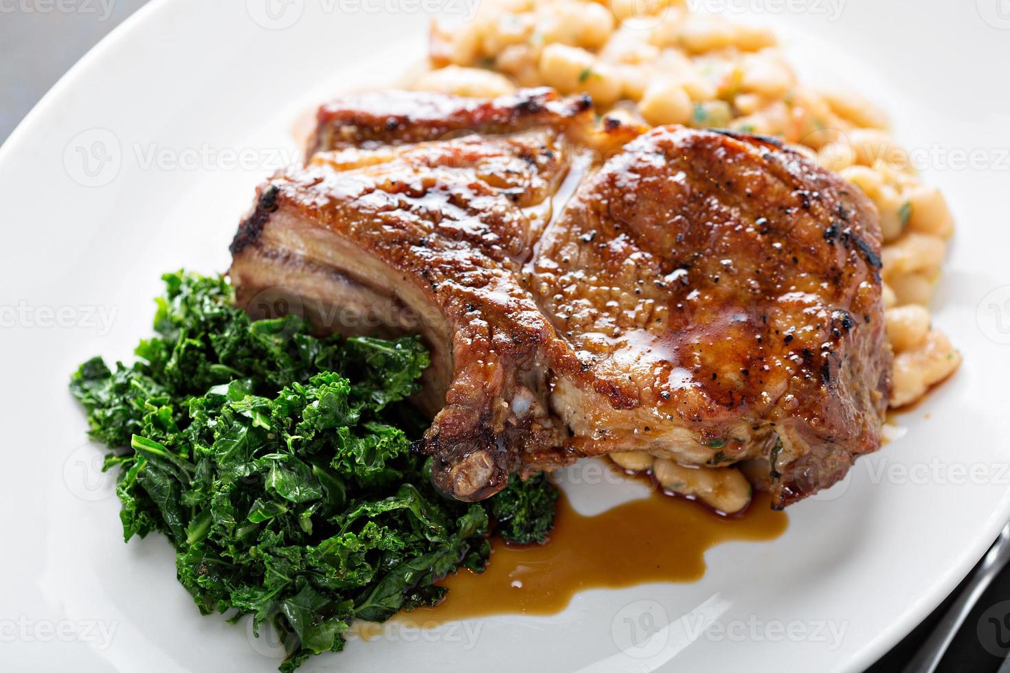 Grilled pork chop with cassoulet and braised greens photo