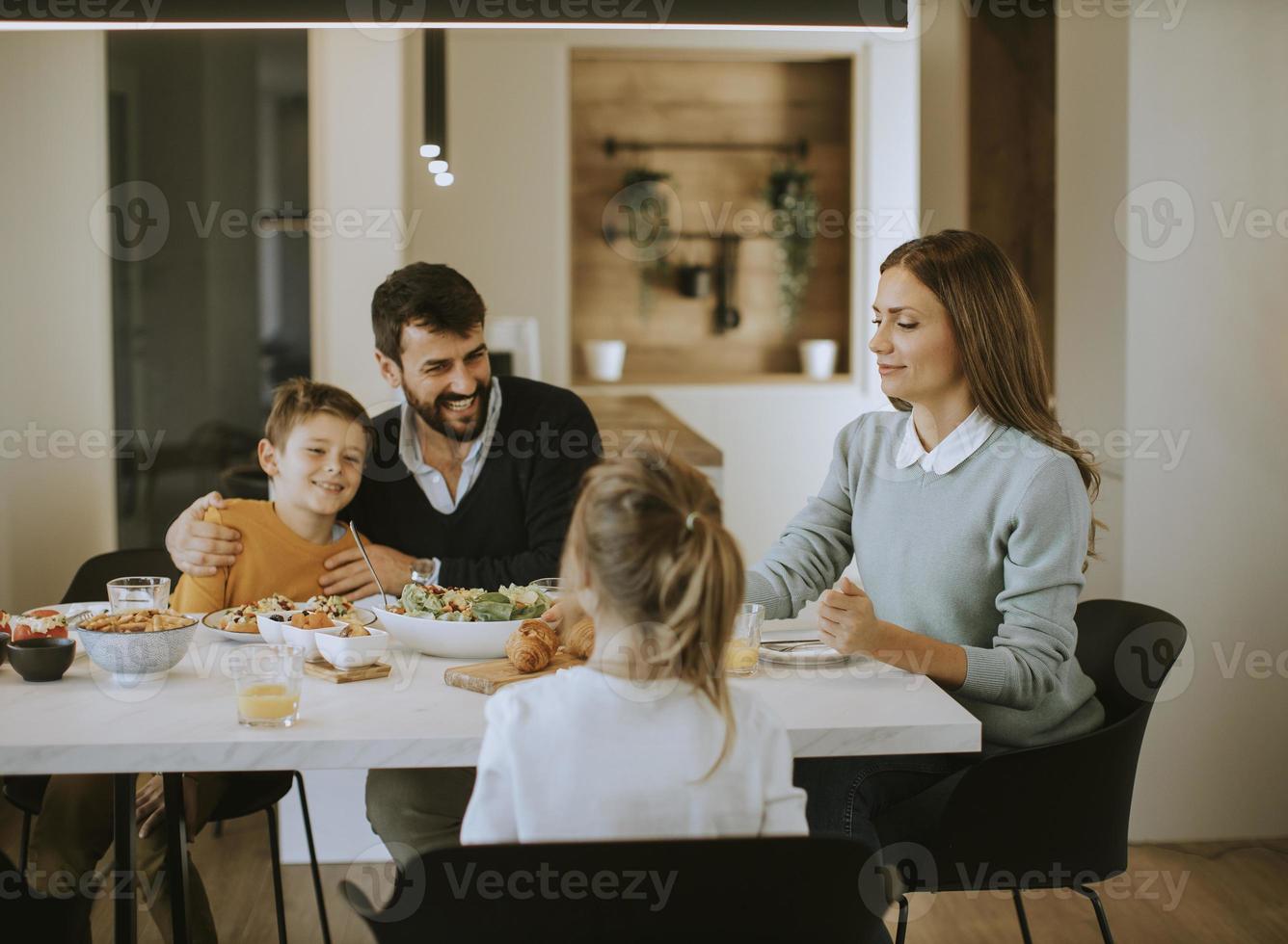 Young happy family talking while having lunch at dining table photo