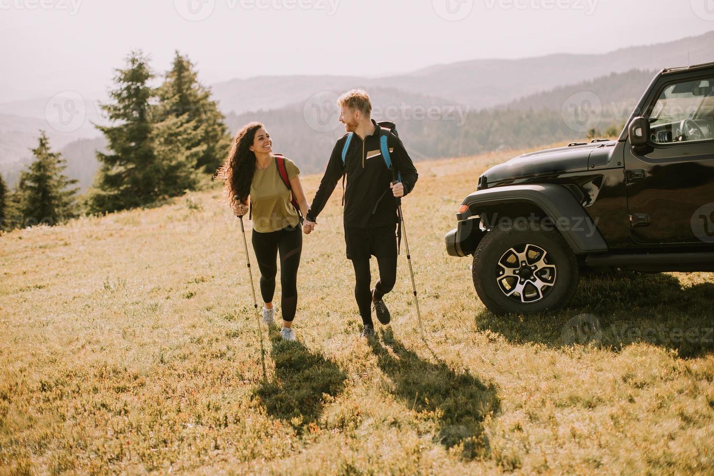 Smiling couple walking with backpacks over green hills photo