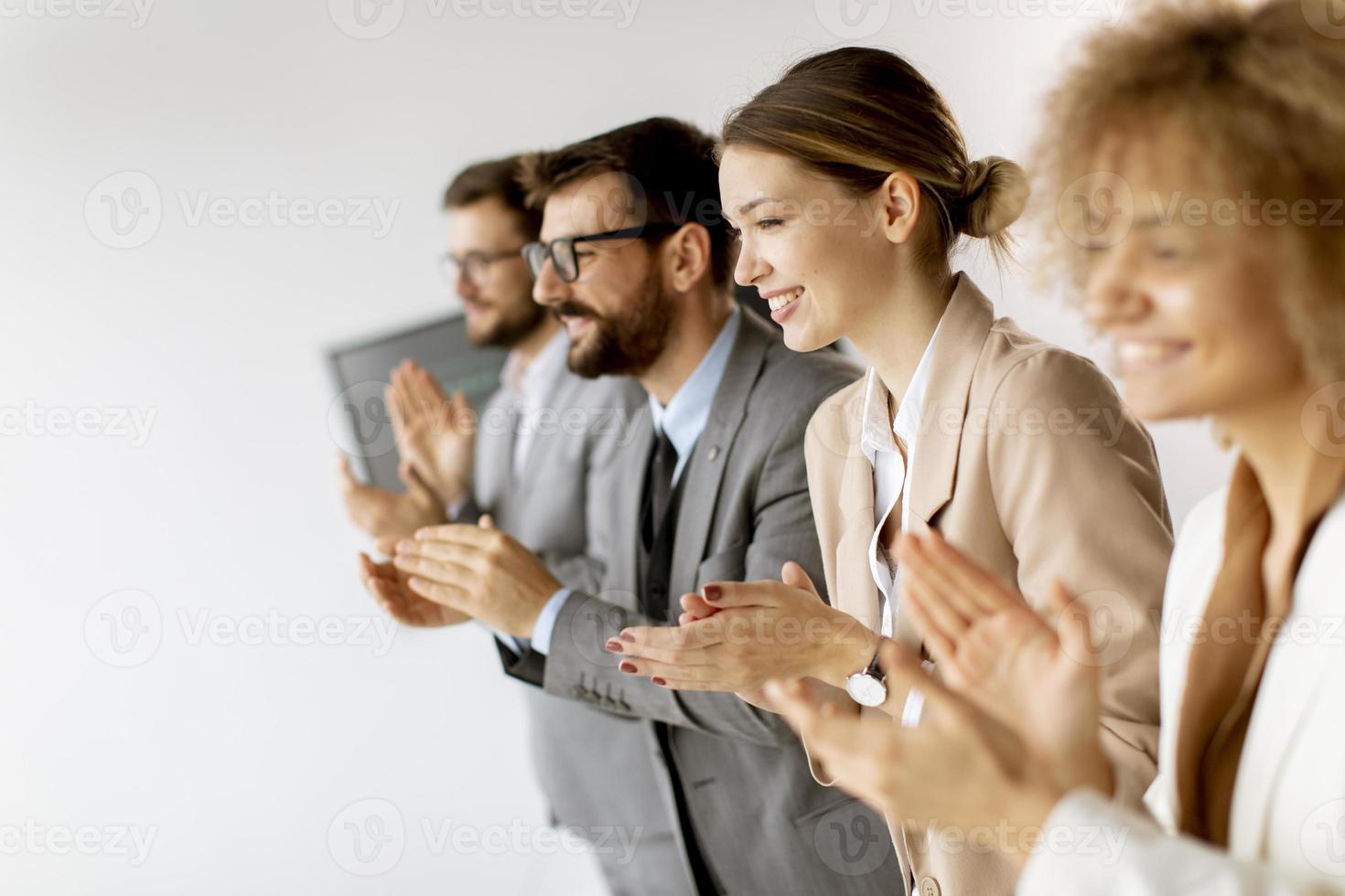 Group of diverse young coworkers standing in a row and applauding at office photo