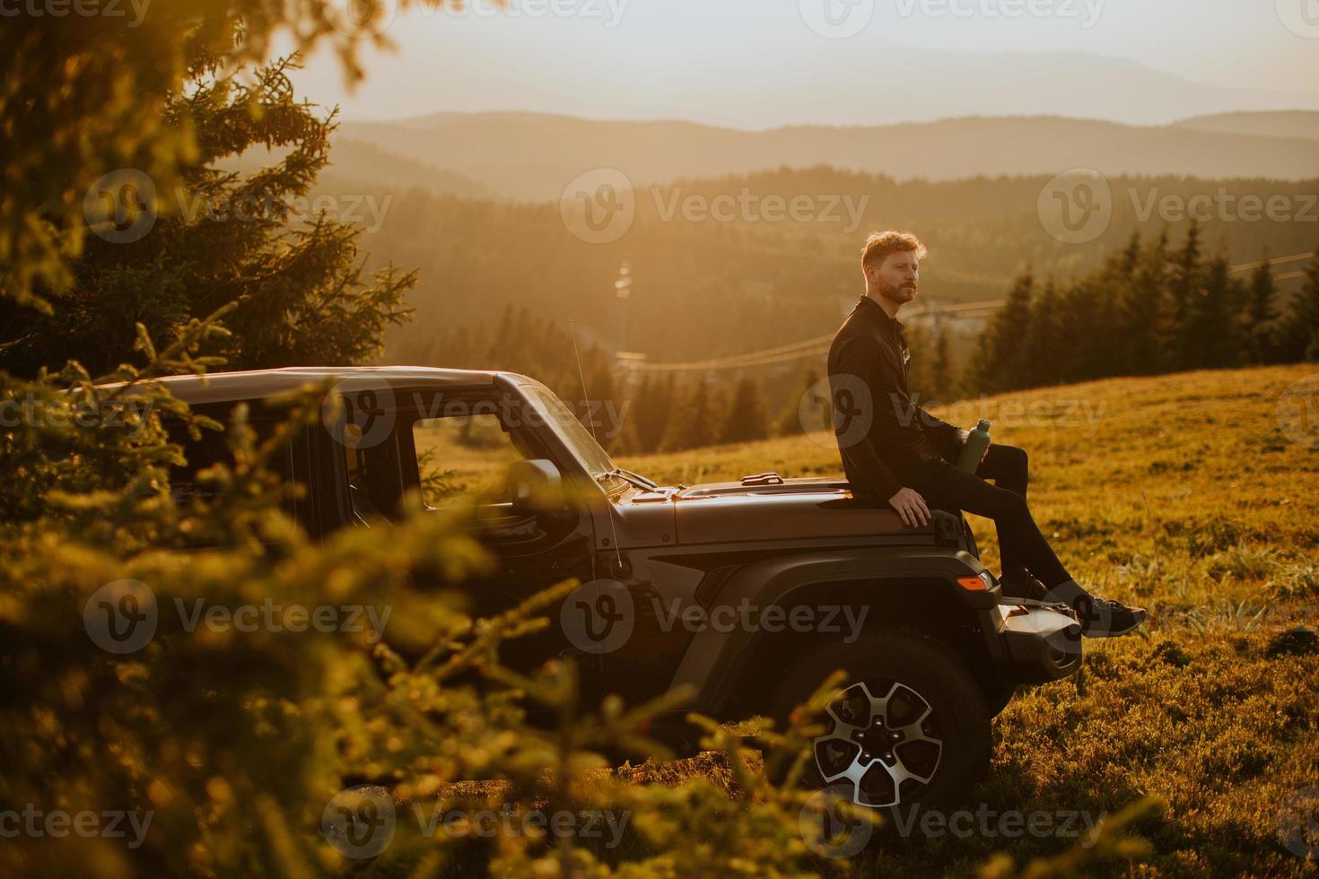 Young man relaxing on a terrain vehicle hood at countryside photo