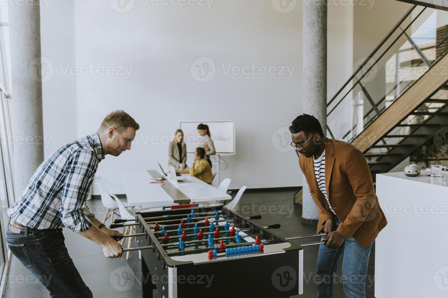 jóvenes empresarios multiétnicos casuales jugando futbolín y relajándose en la oficina foto