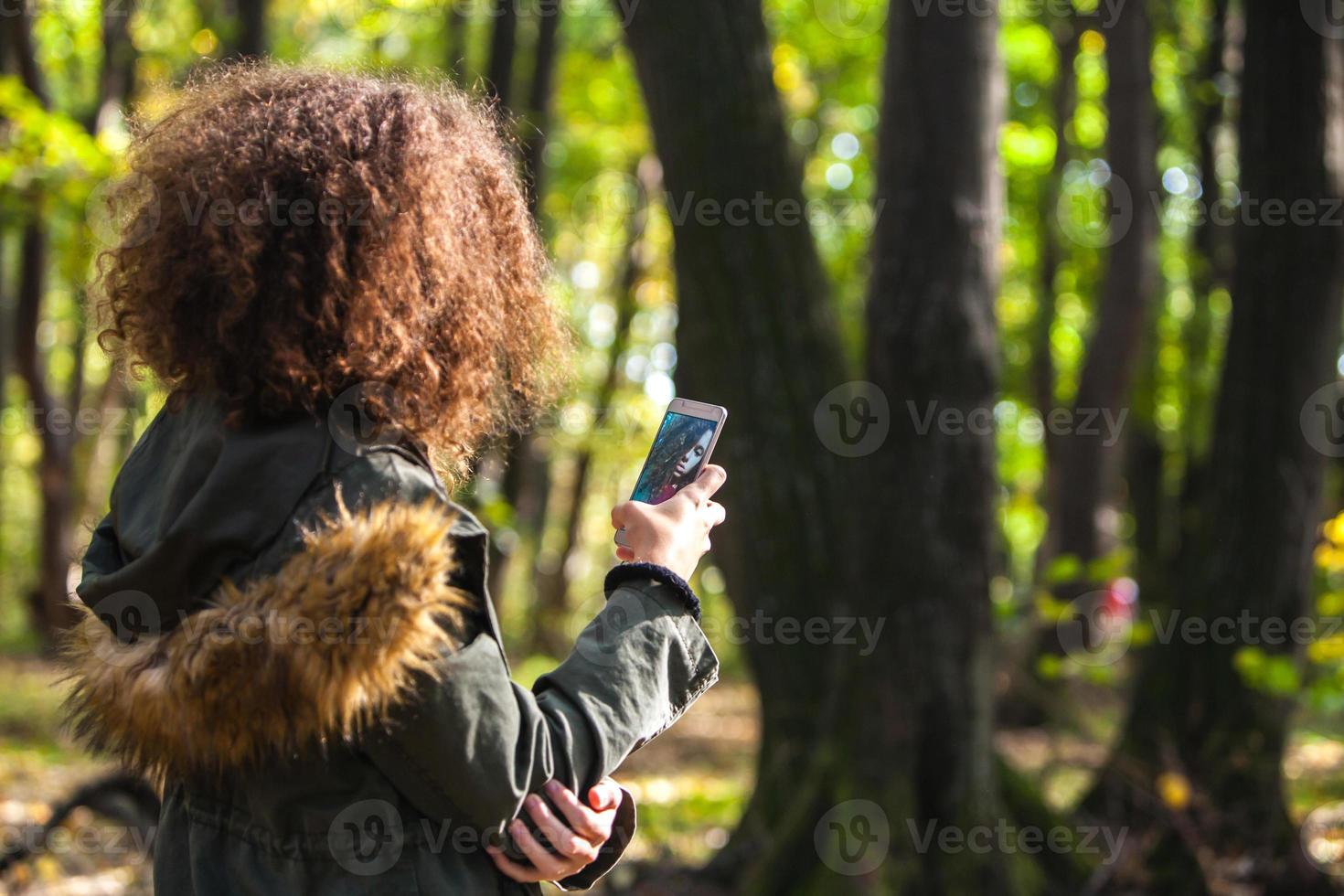 Cute curly hair teen girl with smartphone in autumn forest photo