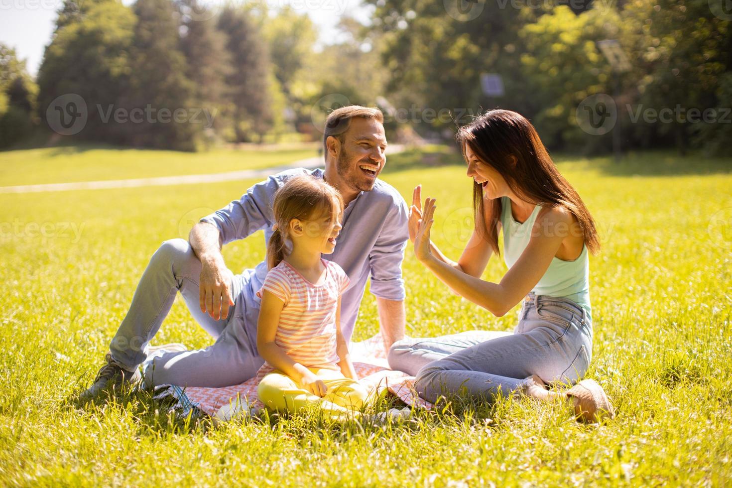 Familia joven feliz con linda hijita divirtiéndose en el parque en un día soleado foto