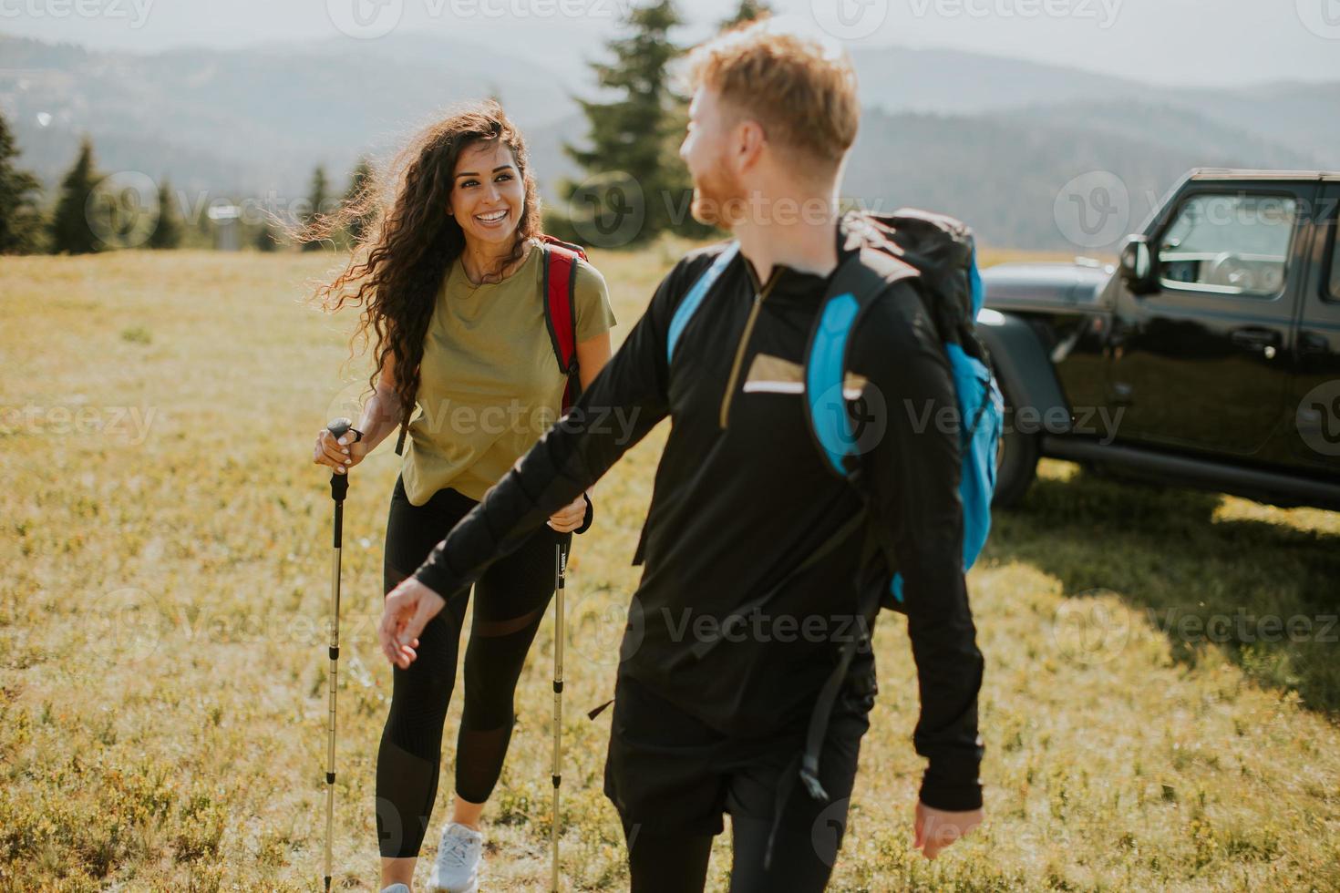 Smiling couple walking with backpacks over green hills photo