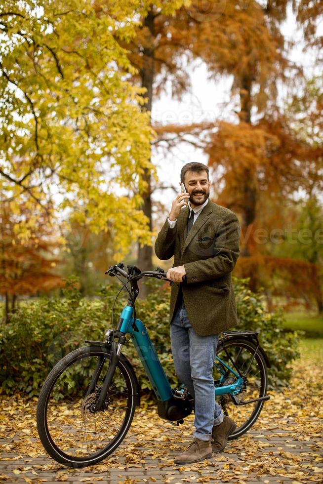 Young man with electric bicycle in the autumn park photo