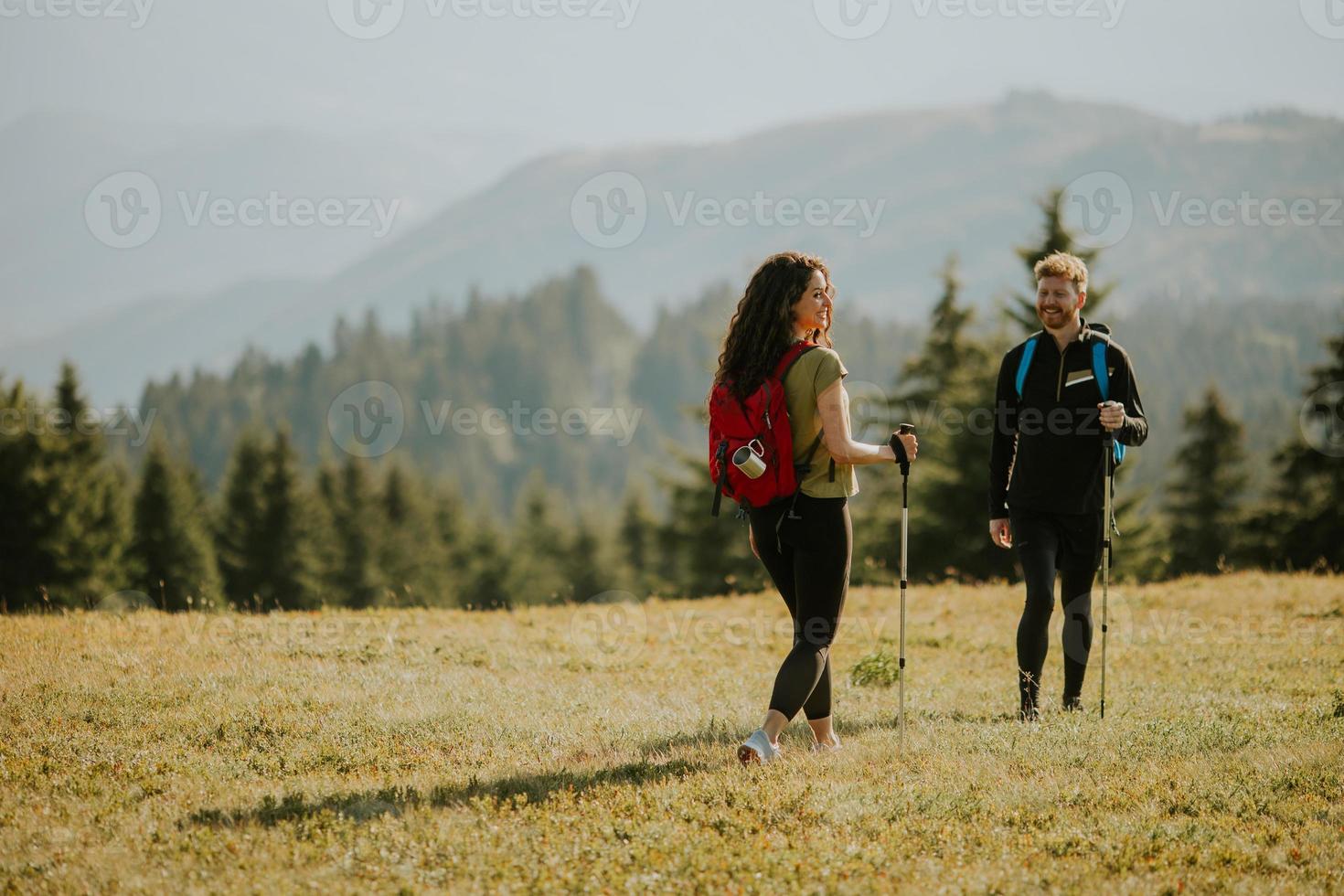 Smiling couple walking with backpacks over green hills photo