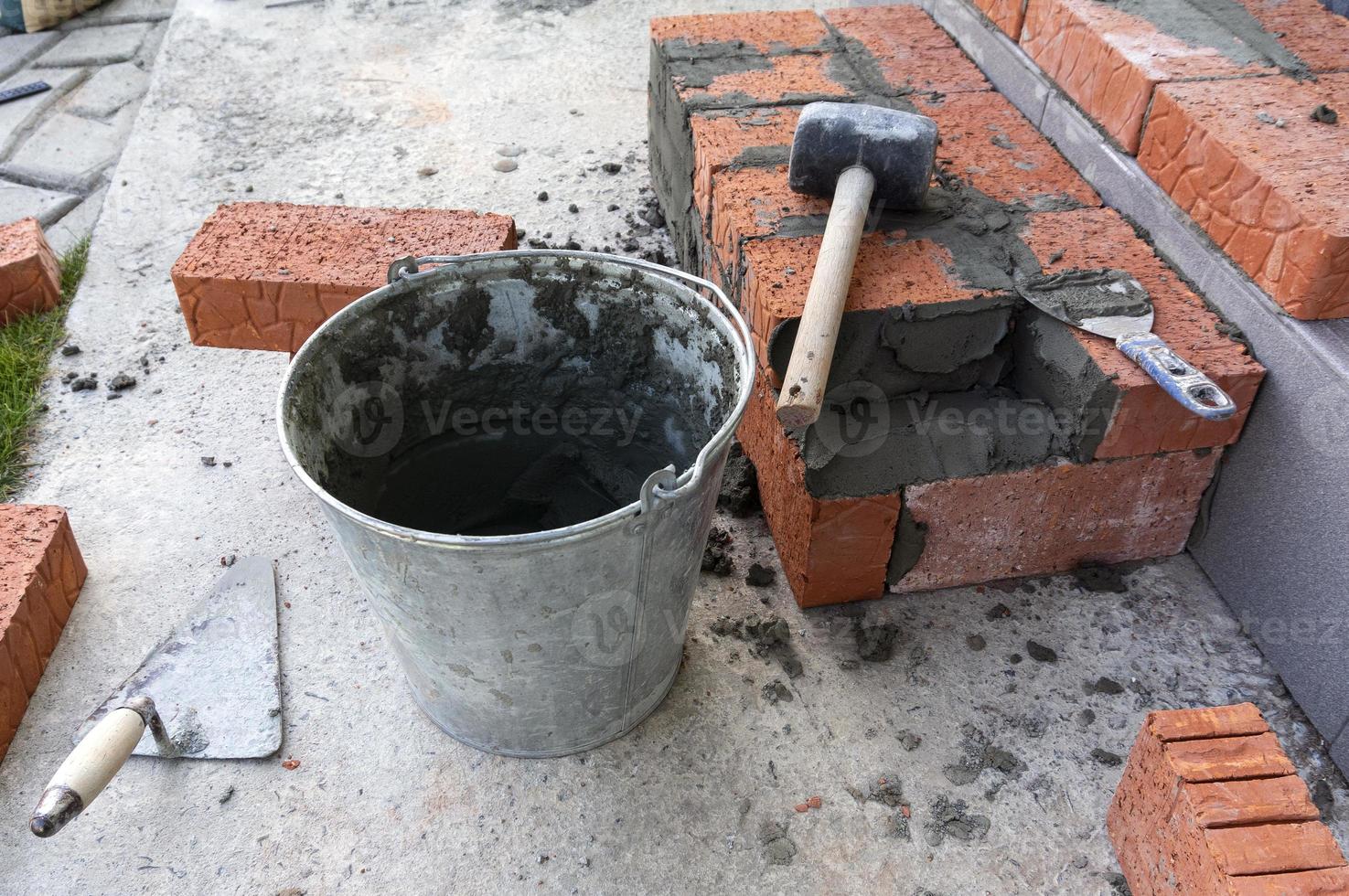 Bucket with a solute, trowel, rubber mallet and clay bricks photo