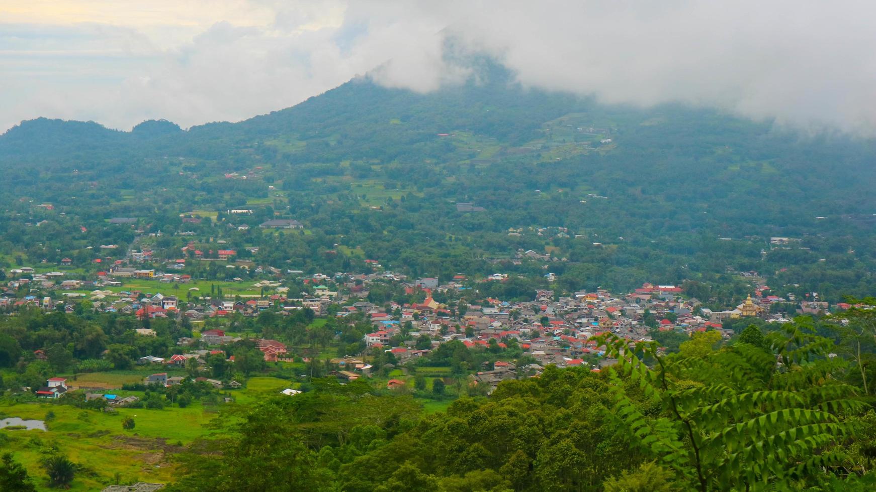 la vista del cielo nublado, árboles, montañas y casas fue fotografiada desde arriba de la colina foto