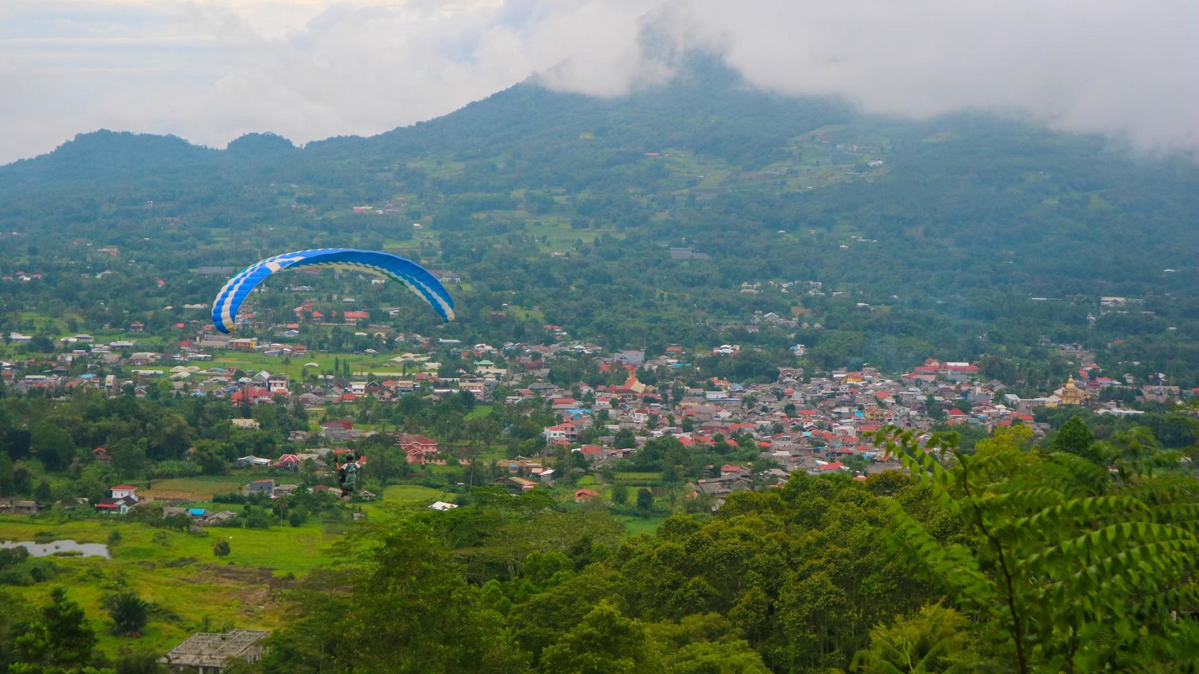 the view of the cloudy sky, trees, mountains and houses was photographed from above the hill photo