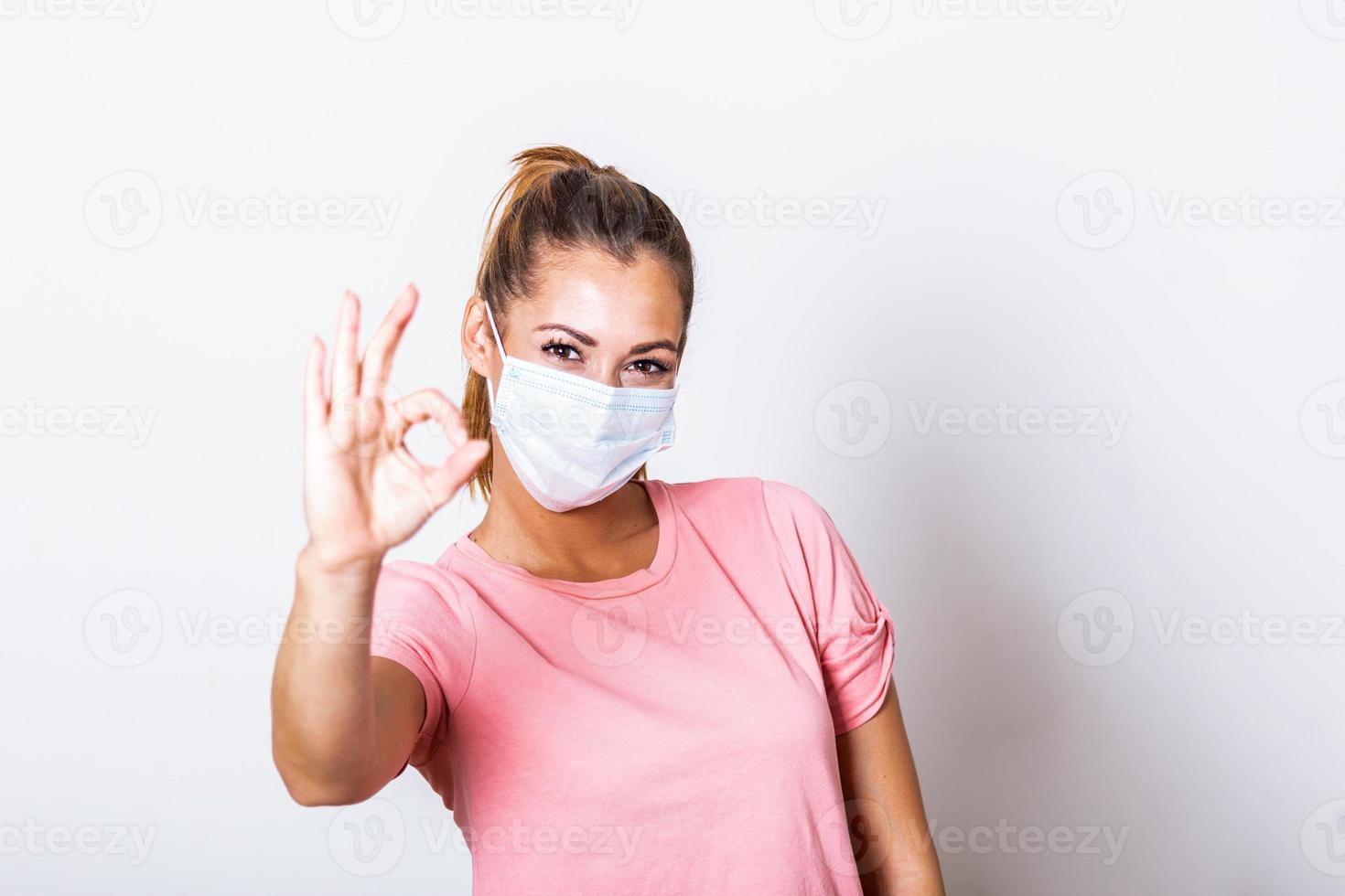 Young woman wearing medical face mask, studio portrait. Woman Wearing Protective Mask and Showing OK sign. Woman wearing surgical mask for corona virus photo