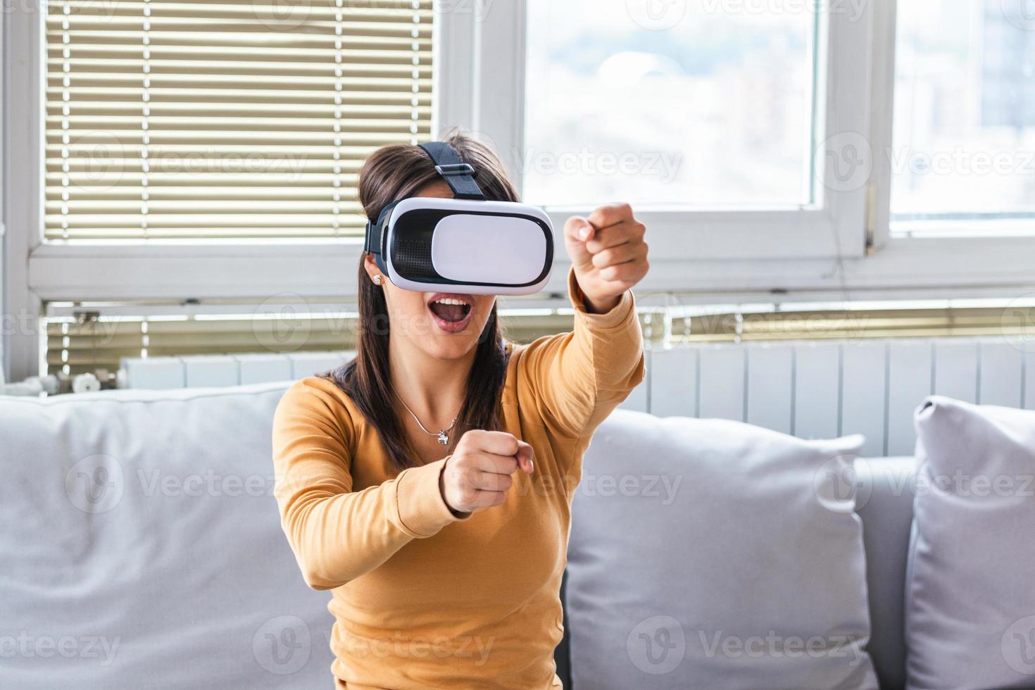 Young elegant woman sitting on sofa chair wearing virtual reality goggles looking online website and using hand moving 3D simulation screen. Enjoying new reality. Attractive young woman in VR headset photo