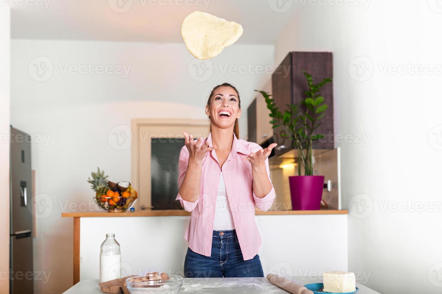 mujer joven lanzando masa de pizza en el aire. mujer joven amasar masa en la cocina, hacer panadería casera. mujer amasando masa en la mesa de la cocina foto