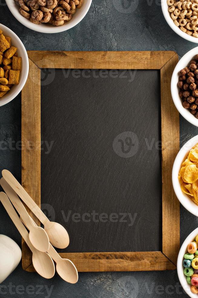 Variety of cold cereals in white bowls around chalkboard photo