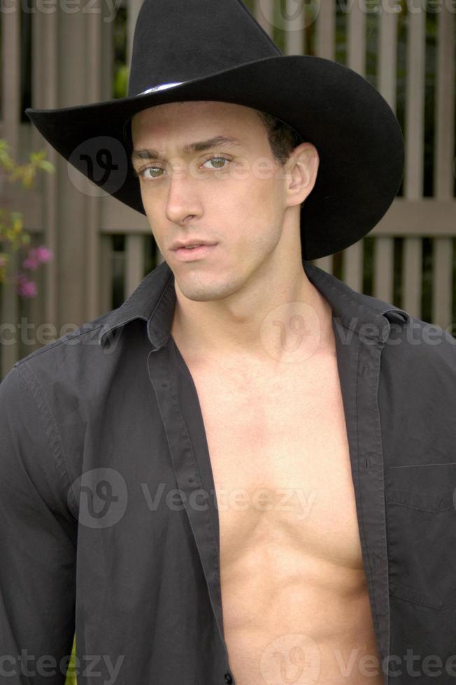 Handsome masculine male cowboy poses for a portrait shot with his shirt open and showing his muscular chest. photo