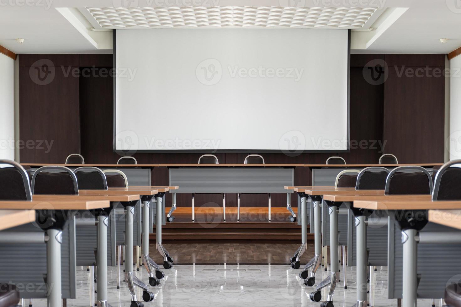 Seminar room with a speaker table in the middle of the stage and whitescreen background photo