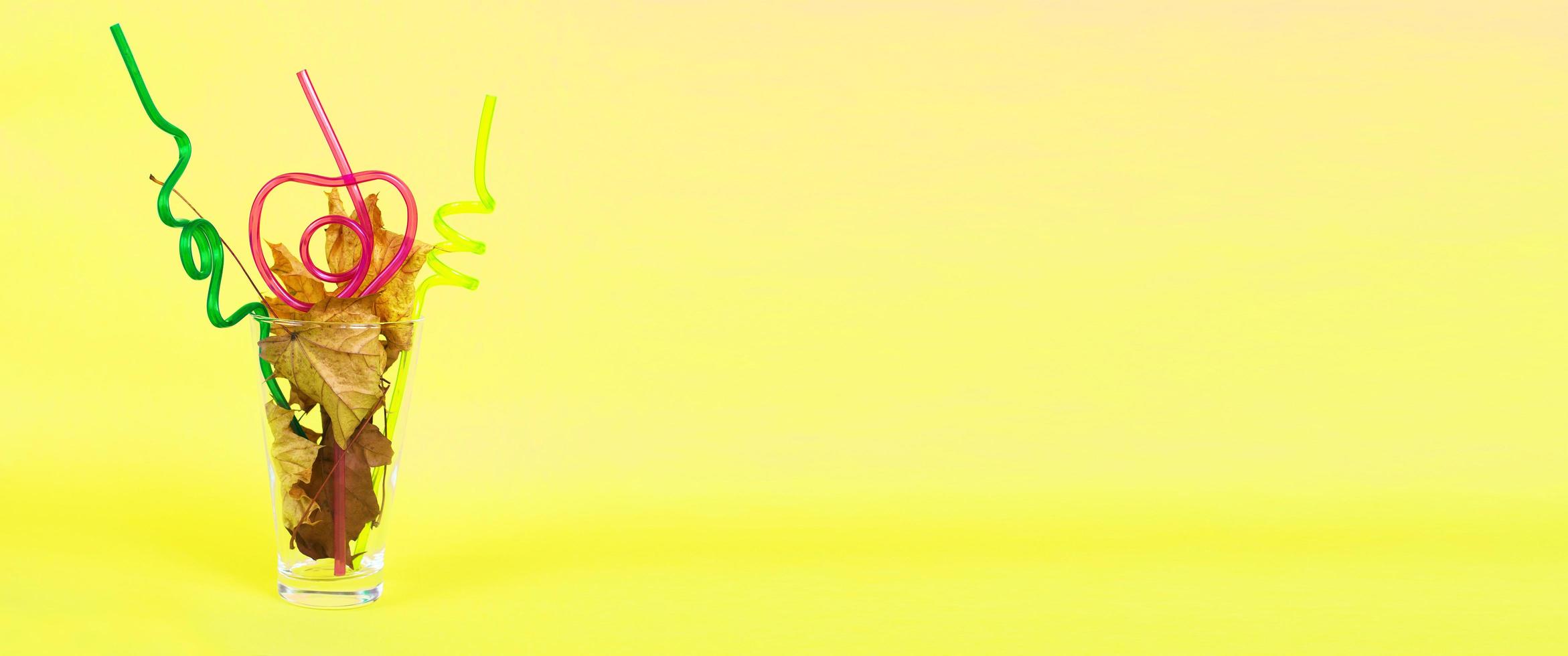 autumn leaf cocktail. autumn leaves in a glass with a straw on a yellow background photo