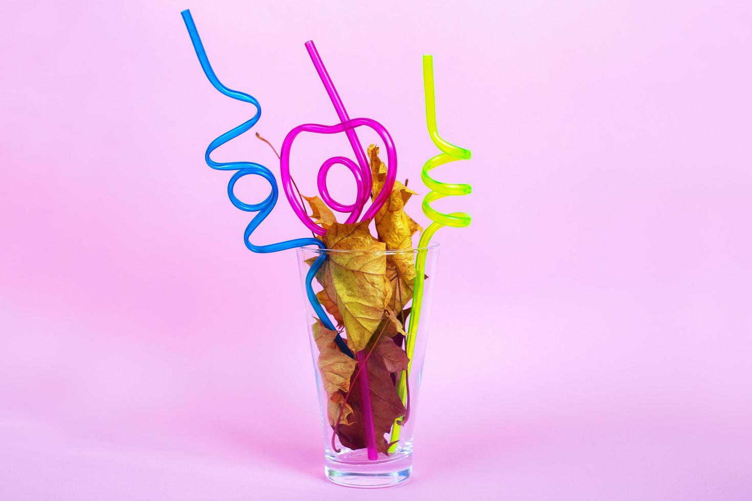 autumn leaf cocktail. autumn leaves in a glass with a straw on a pink background photo