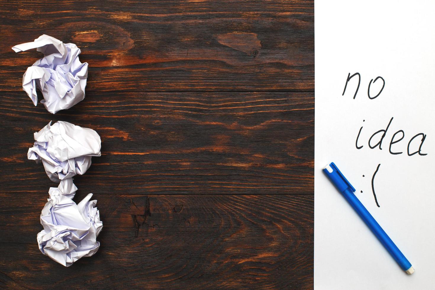 Crumpled up papers with a sheet of blank paper and a pen on wooden background photo