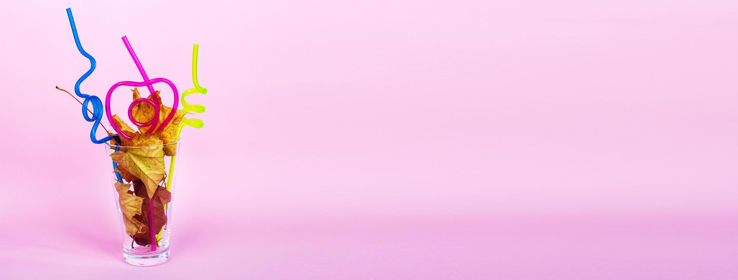 autumn leaf cocktail. autumn leaves in a glass with a straw on a pink background. banner photo