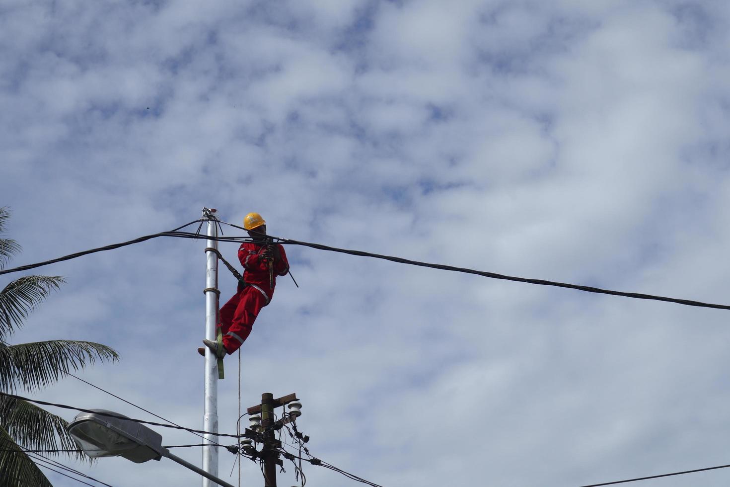 Gorontalo-Indonesia, December 2022 - Technicians connect cables to electric poles. Employee hanging by belt on electricity pole for laying low voltage cable photo