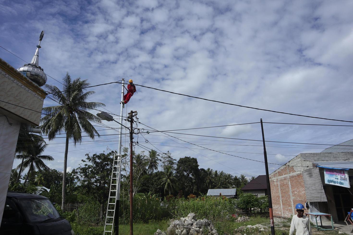 Gorontalo-Indonesia, December 2022 - Technicians connect cables to electric poles. Employee hanging by belt on electricity pole for laying low voltage cable photo