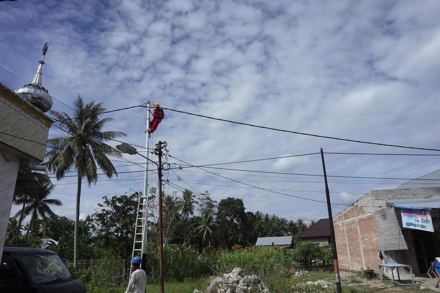 Gorontalo-Indonesia, December 2022 - Technicians connect cables to electric poles. Employee hanging by belt on electricity pole for laying low voltage cable photo