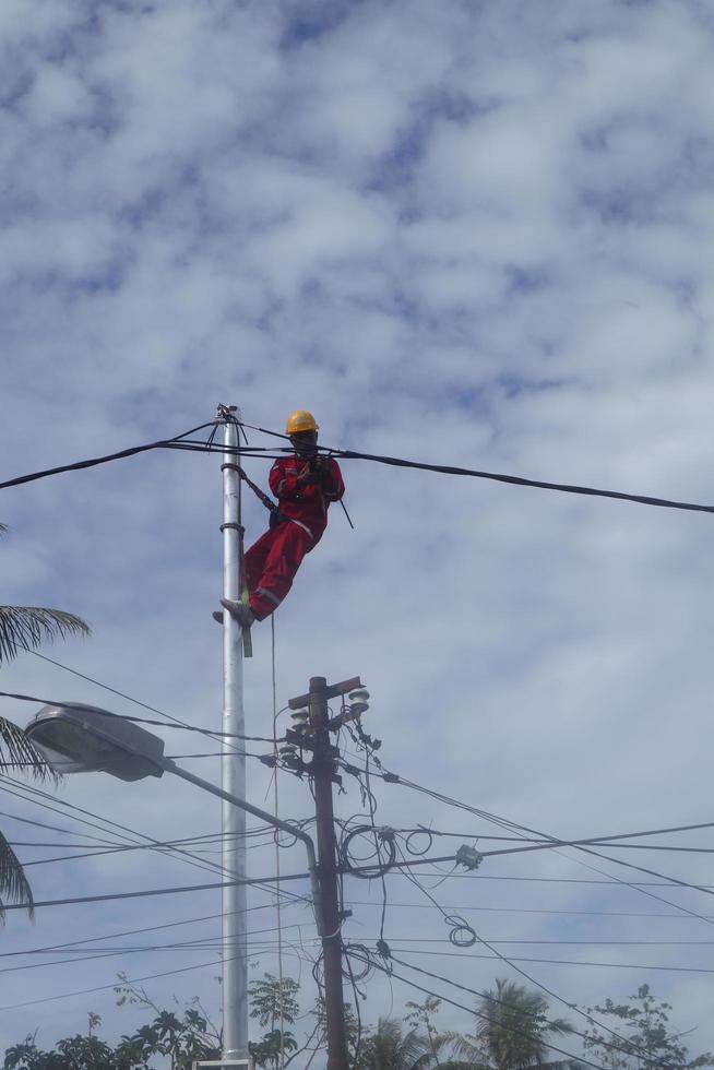 gorontalo-indonesia, diciembre de 2022 - los técnicos conectan los cables a los postes eléctricos. empleado colgando del cinturón en un poste de electricidad para tender un cable de baja tensión foto