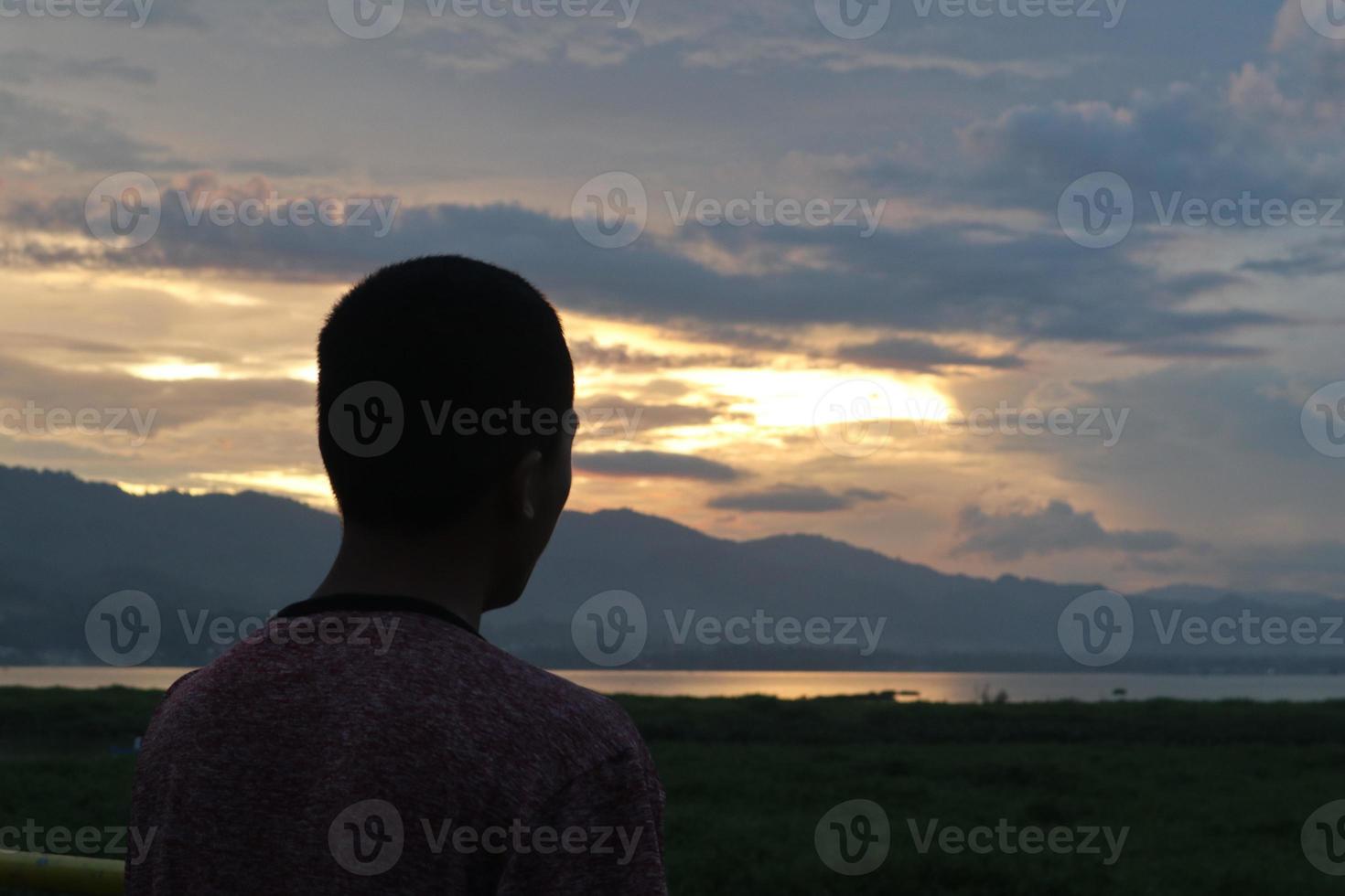 Silhouette of a young man standing by the lake enjoying the sunset. peaceful atmosphere in nature photo