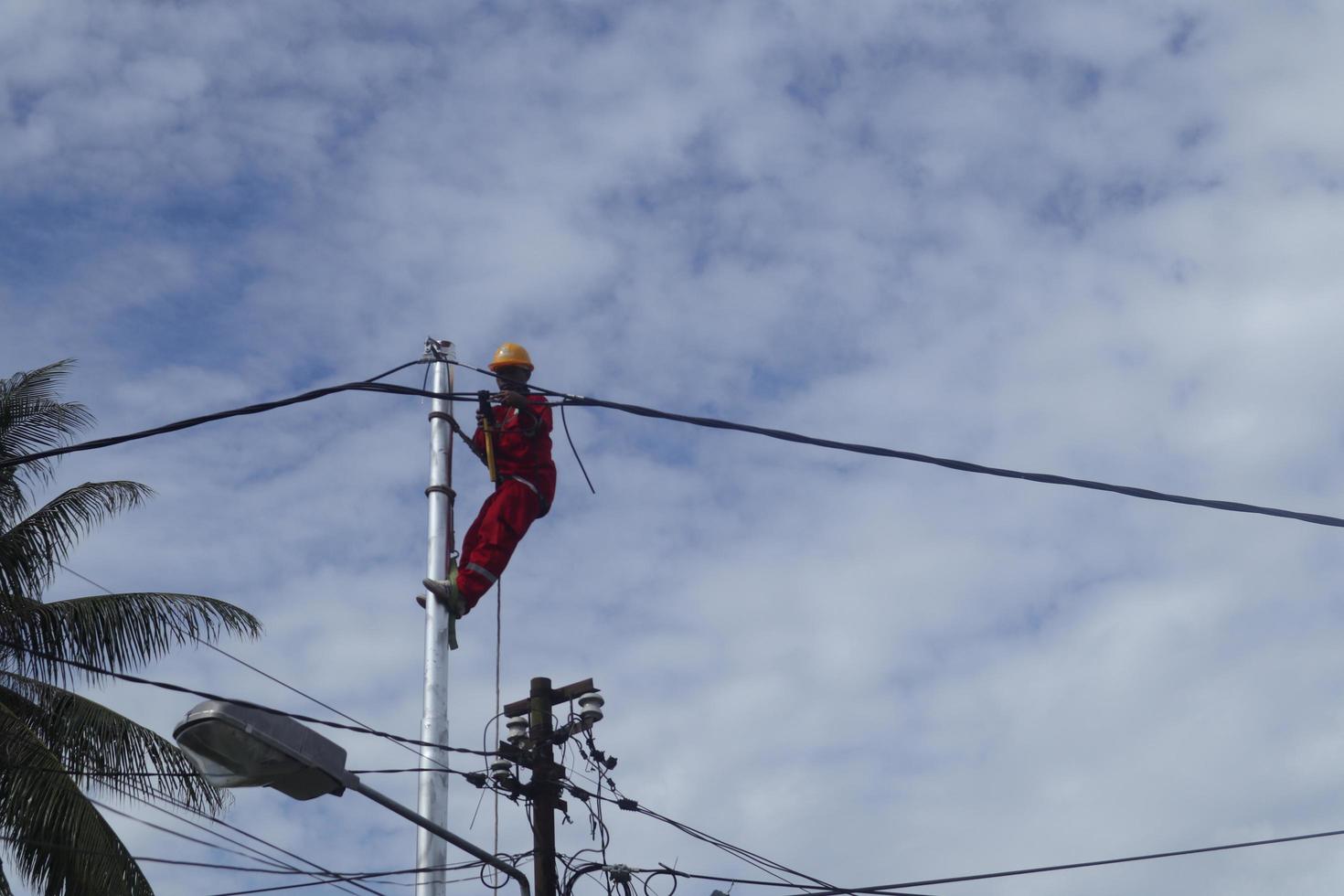 Gorontalo-Indonesia, December 2022 - Technicians connect cables to electric poles. Employee hanging by belt on electricity pole for laying low voltage cable photo
