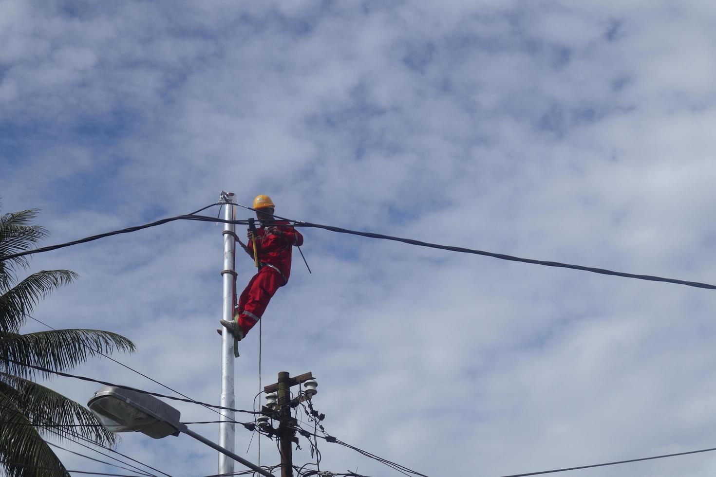 gorontalo-indonesia, diciembre de 2022 - los técnicos conectan los cables a los postes eléctricos. empleado colgando del cinturón en un poste de electricidad para tender un cable de baja tensión foto