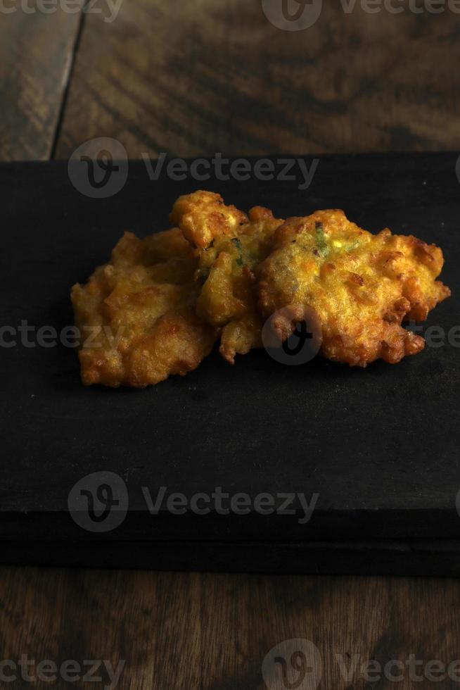 bakwan jagung o buñuelos de maíz está en una tabla de cortar negra contra un fondo de madera foto