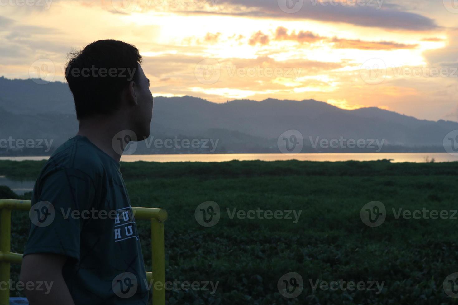 Silhouette of a young man standing by the lake enjoying the sunset. peaceful atmosphere in nature photo