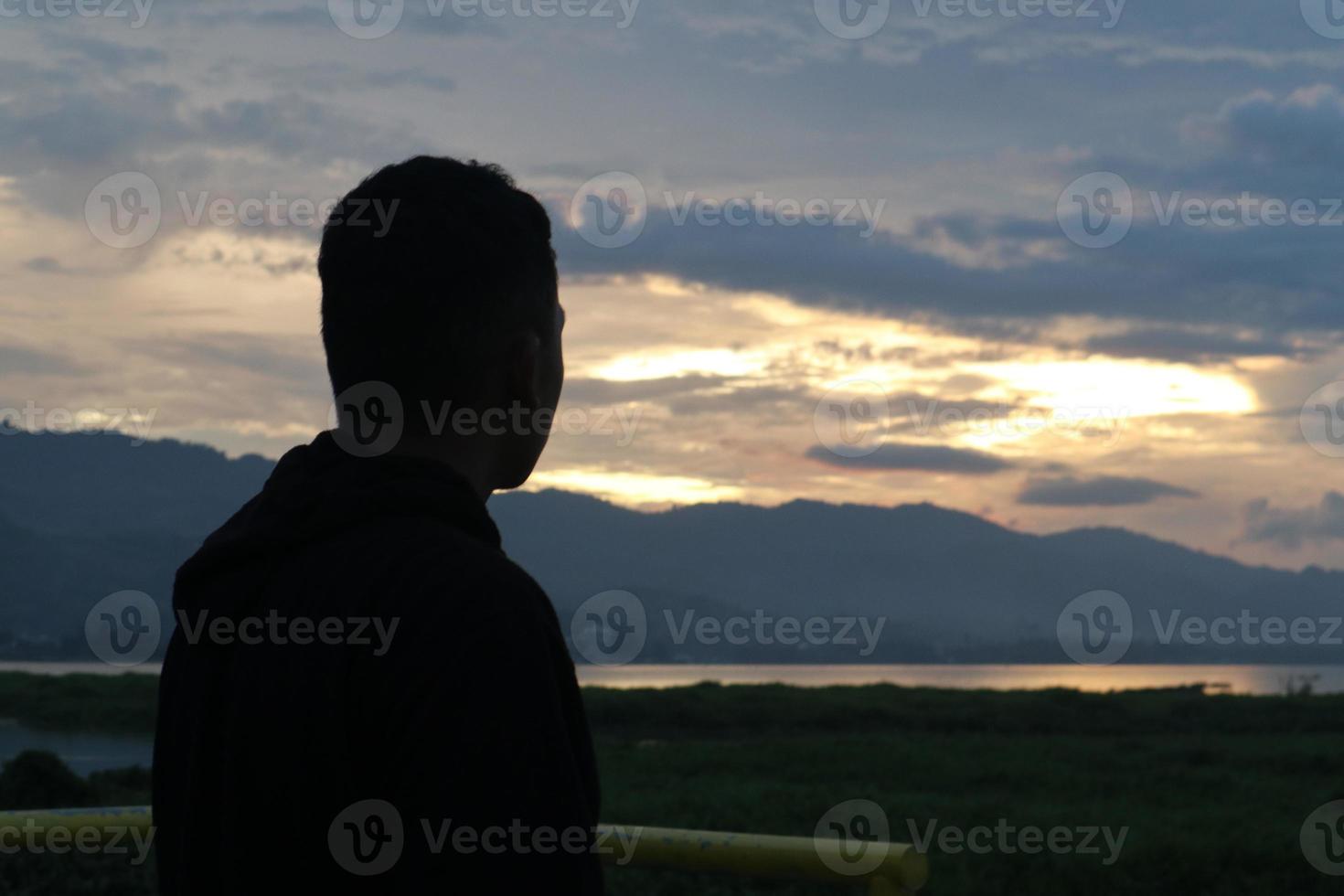 Silhouette of a young man standing by the lake enjoying the sunset. peaceful atmosphere in nature photo