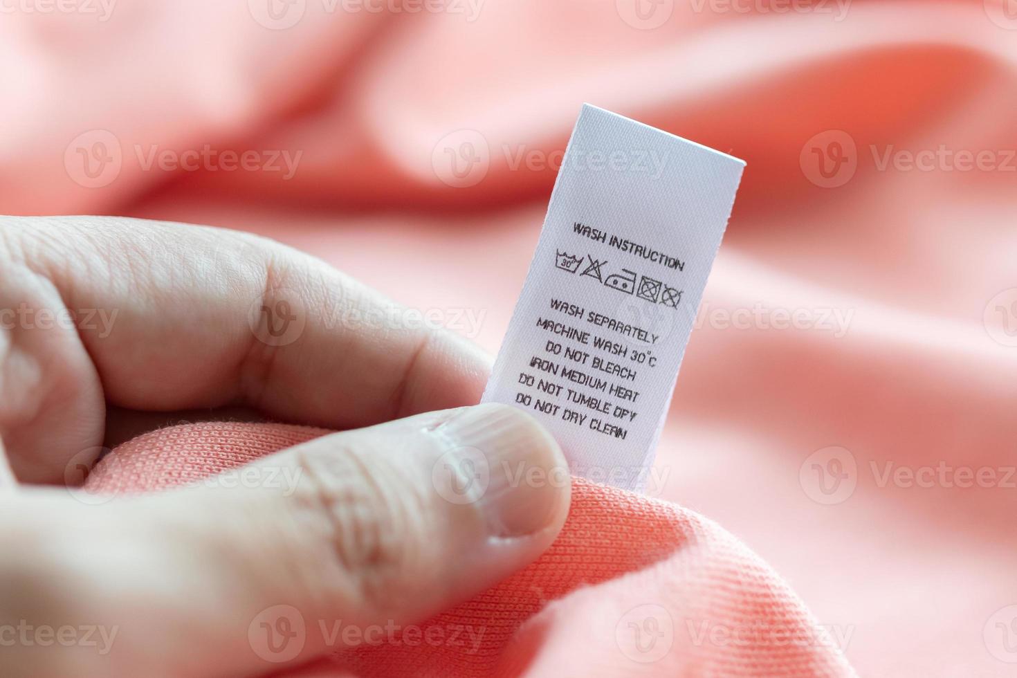 Hand hold and reading at white laundry care washing instructions clothes label on pink shirt photo