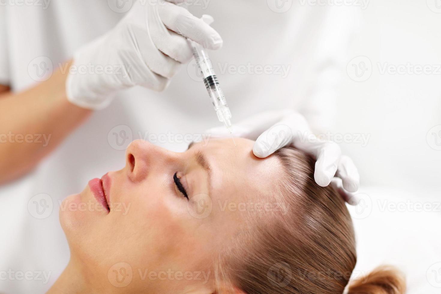 Close up of hands of cosmetologist making botox injection in female forehead photo