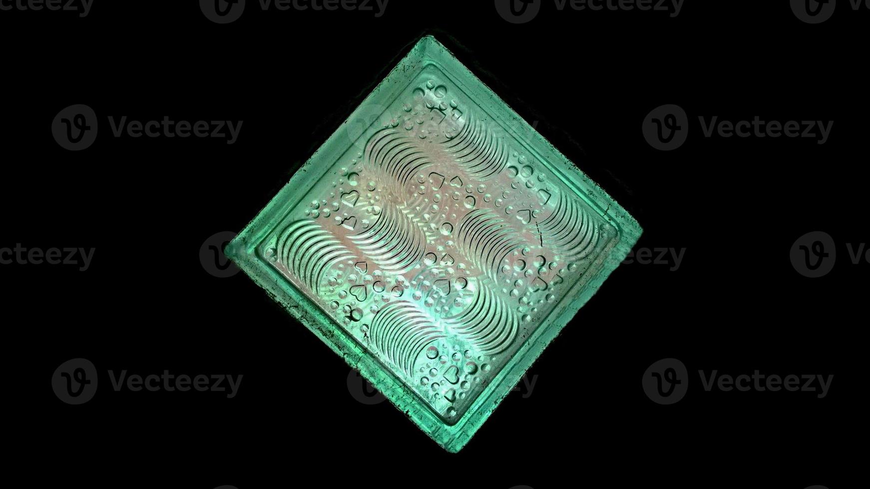Green glass decorates house with low light techniques, surface of carved glow transparent squares tile pronounced pattern. Selective focus black background. photo