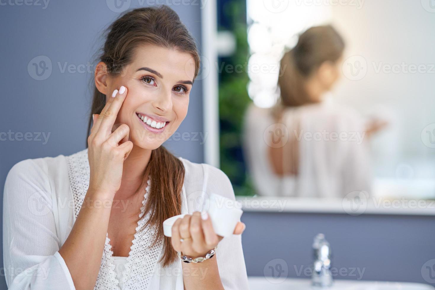 Beautiful brunette woman applying face cream in the bathroom photo