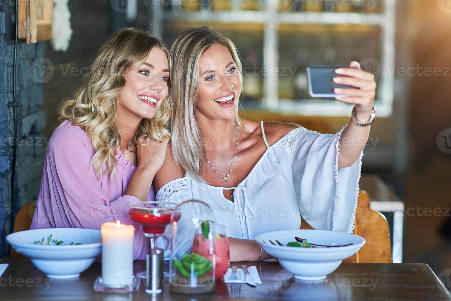 Two girl friends eating lunch in restaurant and using smartphone photo