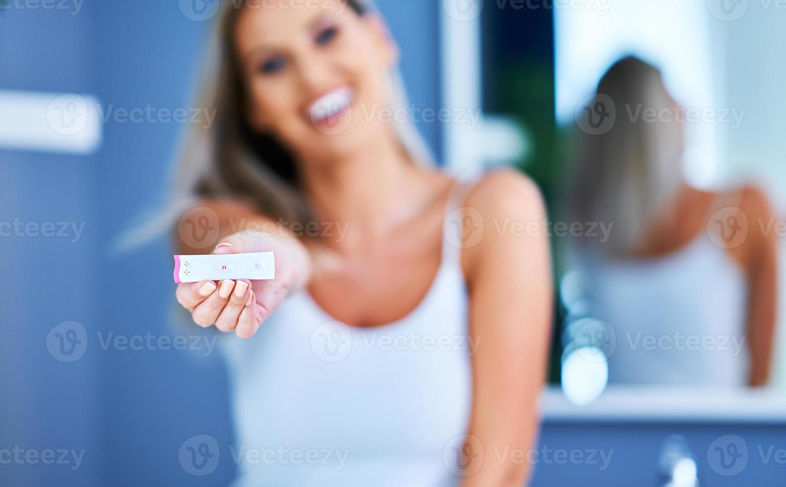 Happy young woman looking on pregnancy test in bathroom photo