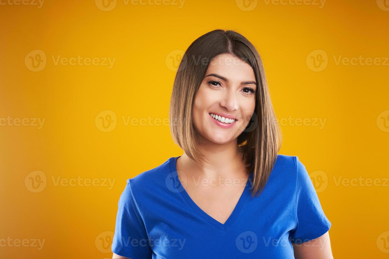 Close up of woman in blue t-shirt looking at camera over yellow background photo