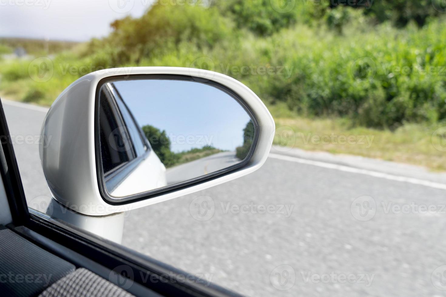 Mirror view of white car travel on the asphalt road. with blurred of green grass at day. photo