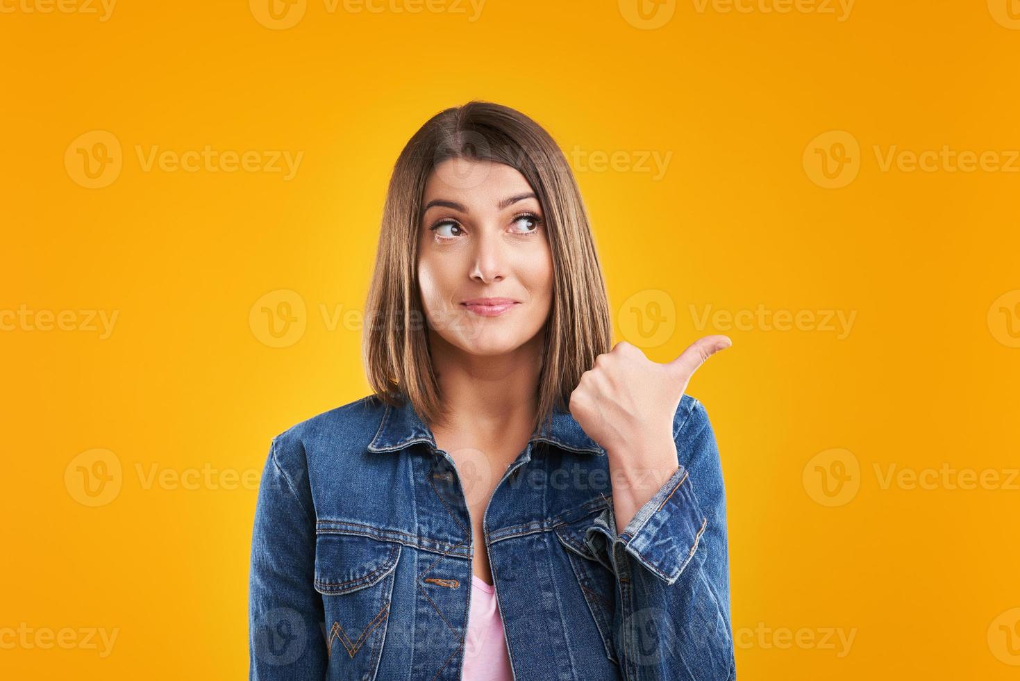 Close up of woman in denim jacket thinking and pointing over yellow background photo