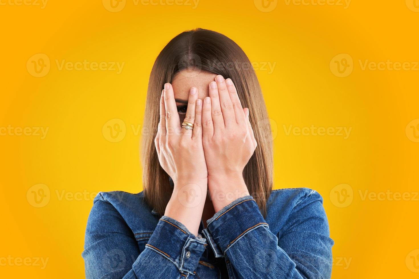 Unhappy woman in denim jacket over yellow background photo