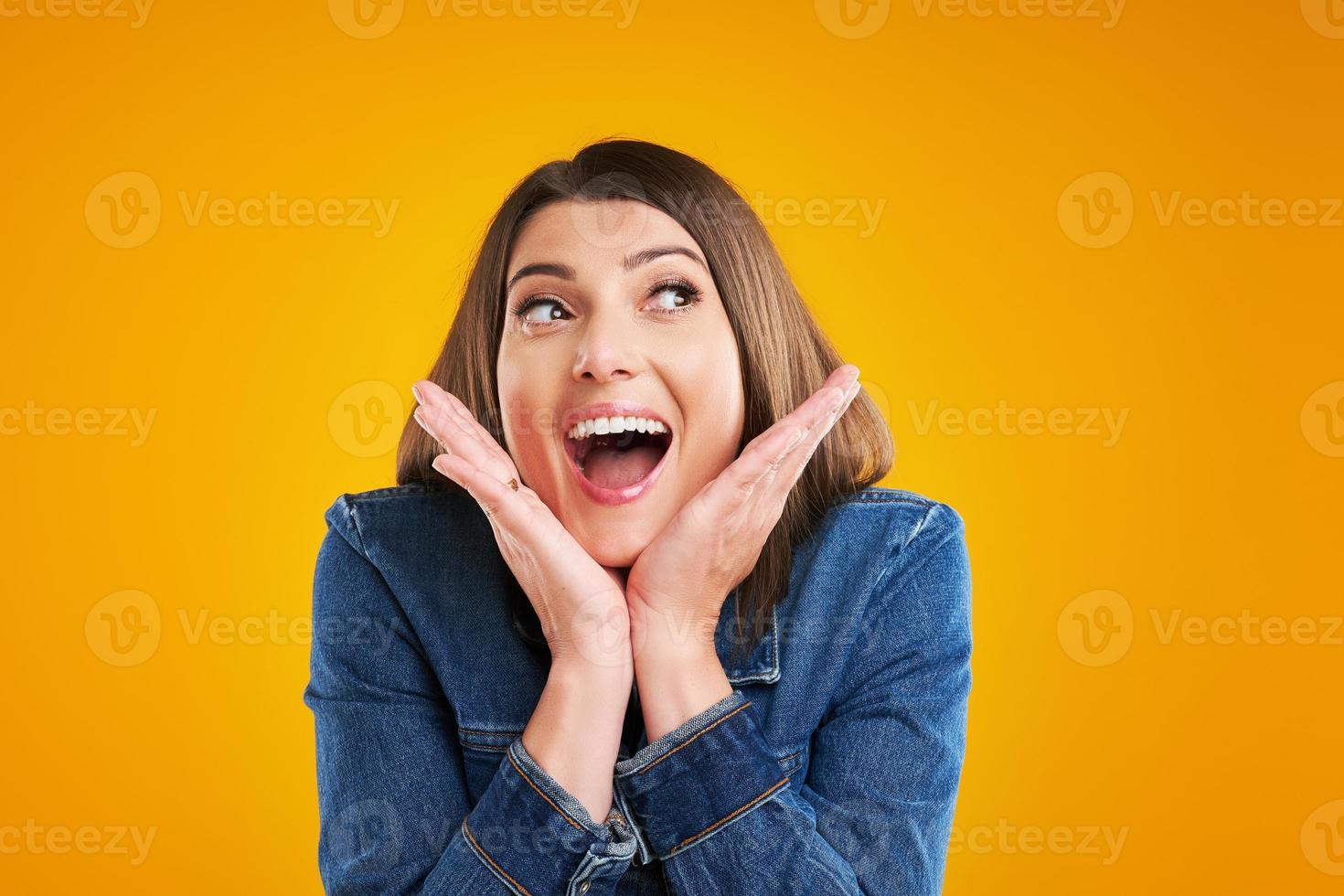 Close up of woman in denim jacket thinking and pointing over yellow background photo