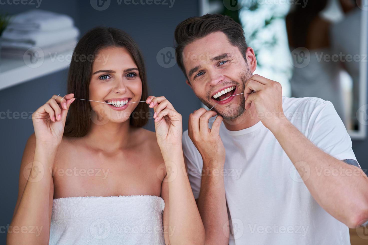 Portrait of happy young couple flossing teeth in the bathroom photo