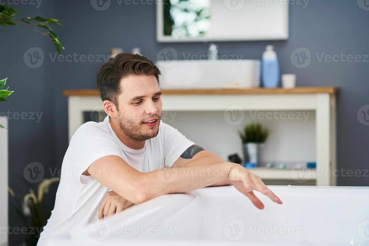 Adult man preparing bath in the bathroom photo