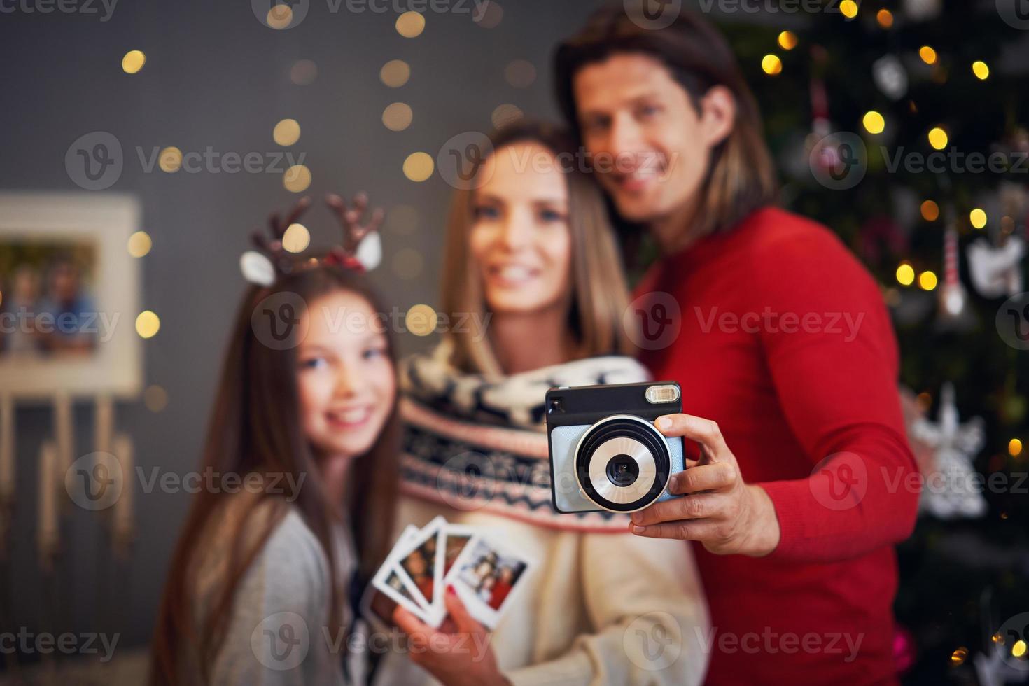 Beautiful family celebrating Christmas at home and taking instant pictures photo