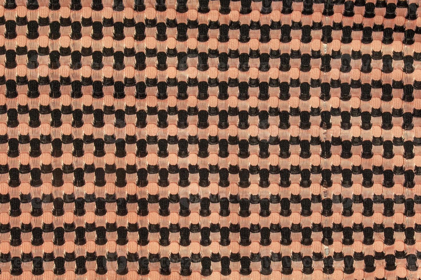 The background of a knitted fabric is orange-black with a regular geometric pattern. Openwork finely knitted woolen fabric. photo
