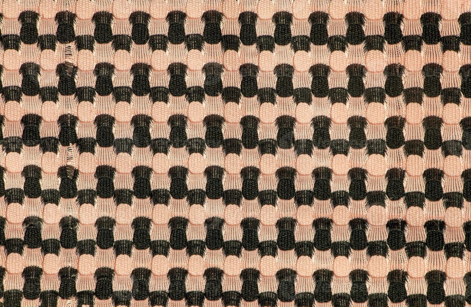 The background of a knitted fabric is orange-black with a regular geometric pattern. Openwork finely knitted woolen fabric. photo